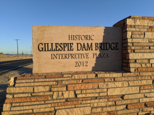 Sign for the Historic Gillespie Dam Bridge Interpretive Plaza, made of stone, with a clear blue sky in the background.